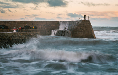 Waves hitting the stone wall in Cove Harbour, Scotland, with evening light and a man standing on the sea wall. Long Exposureの写真素材