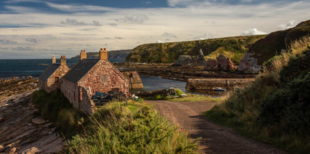 Small harbor in the village of Cove, east coast of Scotland, with two fishermen houses and a stone dock. Surrounded by grassy cliffsの写真素材