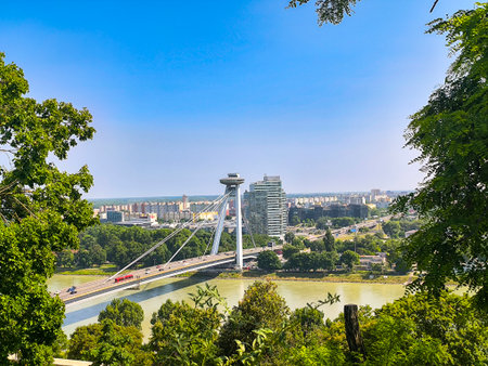 View from castle hill of Most SNP bridge and UFO tower over Danube River and framed by green trees on a sunny day in Bratislava, Slovakiaの写真素材