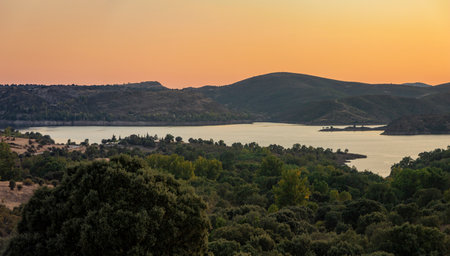 Landscape view of Alcorlo, water reservoir in Guadalajara, Spain. At sunset, with orange sky and surrounded by woodland and hillsの写真素材