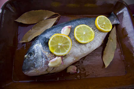 Sea bream in a pan with garlic and lemon slices.