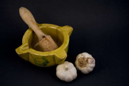Displays a ceramic mortar with pestle and garlic.