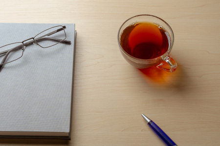 Gray diary, cup of tea, blue pen and glasses on a brown table, selective focusの写真素材