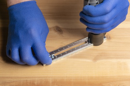A man in blue gloves is cutting a hole in a sheet of plywoodの写真素材