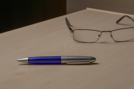 Blue pen and glasses on the office brown desk, selective focusの写真素材