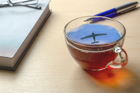 A cup of tea with a reflection of the aircraft in the sky on the office deskの写真素材