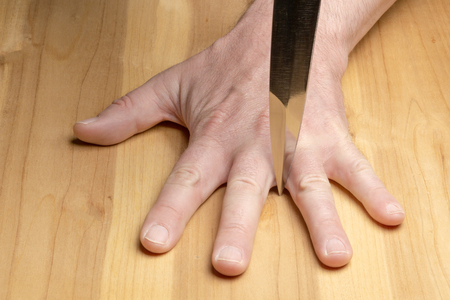 Dangerous game. Blade of the knife between the fingers on the background of a wooden tableの写真素材