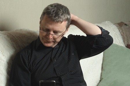 A man in a black shirt reads a message in the smartphoneの写真素材