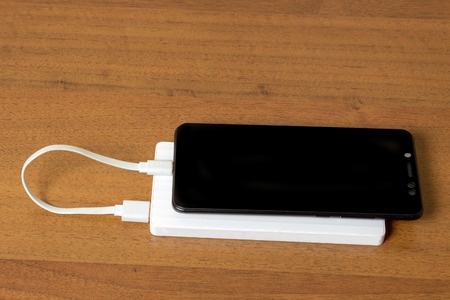 Black smartphone charging with white Power Bank through USB Cable, top view
