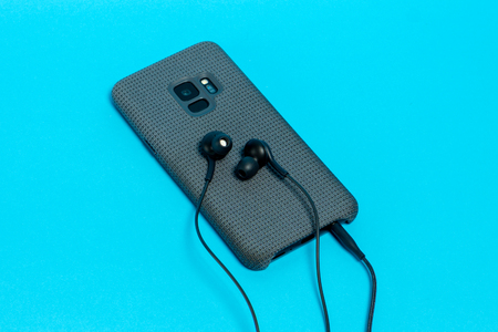Smartphone in stylish textile case with connected headphones on blue backgroundの写真素材