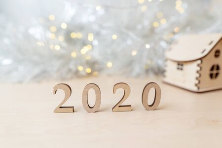 2020 happy new year wood number and a wooden house with a blurry garland in the background. Copy...