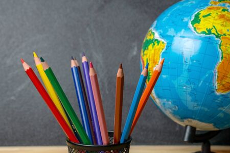 Colored pencils and a globe on the background of the blackboardの写真素材