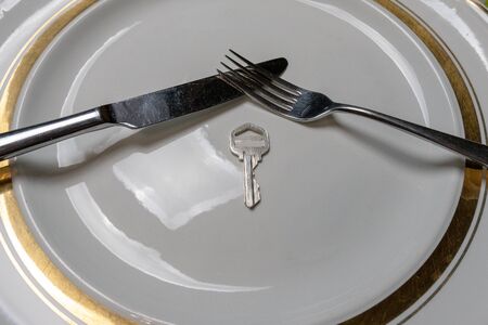 Key on a plate with a knife and fork. Key and cutlery on a white plate. The concept of proper and healthy nutritionの写真素材