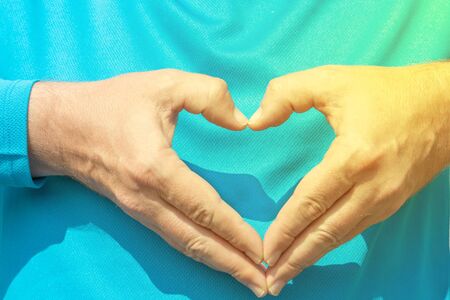 Mens hands in the form of a heart are folded on the chest. A man in a blue sweater shows a heart...