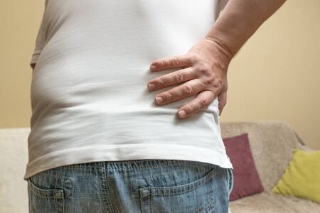 Close up of a man holding his back in pain. A man holding on to his back in the living room