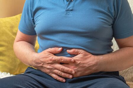 A man in a blue T-shirt holds his hands on his stomach.の写真素材