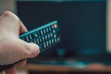 Male hand with a TV remote control close-up. The man turns on the TV. Soft focus.の写真素材