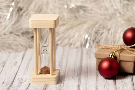 Hourglass and cardboard box on a wooden table decorated with a garland and red Christmas balls for...