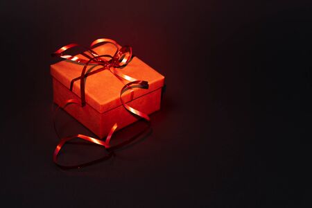 Gift box with a red ribbon on a dark background. Red backlightの写真素材