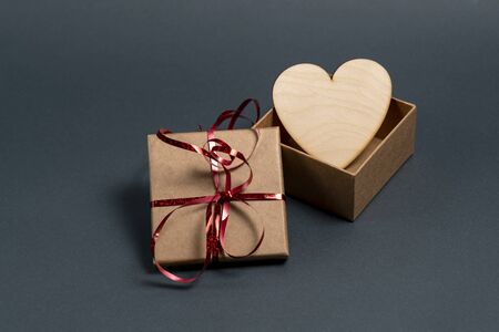 Gift box with red ribbon and a wooden heart on a gray background. Soft focus.