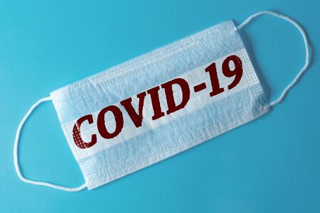White medical mask with the inscription COVID-19, blue backgroundの写真素材