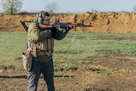 White man in military uniform shoots an AK at a shooting rangeの写真素材