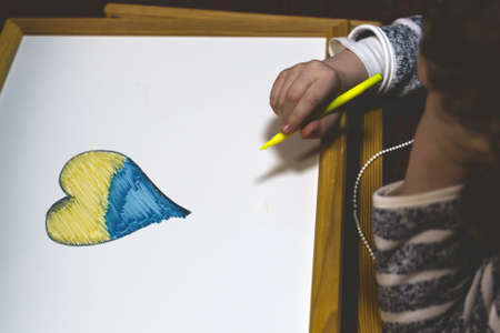 Ukrainian flag and a heart in yellow and blue color. Child draws a heart on the blackboardの写真素材