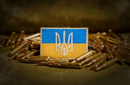 Patch with the flag and coat of arms of Ukraine, rifle cartridges on a camouflage background. Selective focus on patch, macroの写真素材