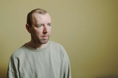 Portrait of a young man in a gray sweater on a yellow background.