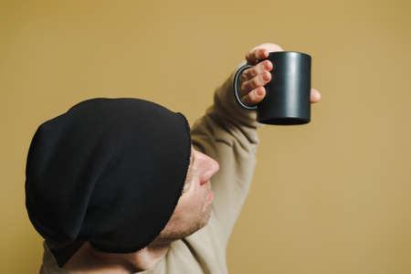 A man looks in surprise into an upside down black cup. Portrait of a young man in a black cap.の写真素材