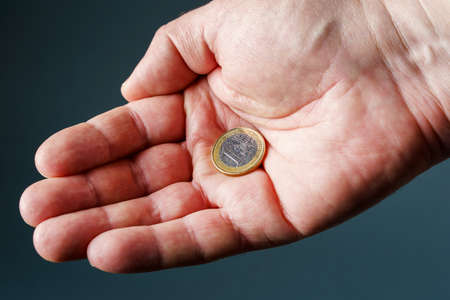 one euro coin in male palm, gray background close-up.
