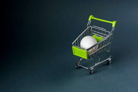 white chicken egg in a small shopping cart on a gray background, close-up.の写真素材