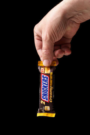 Chocolate bar Snickers in a man's hand close-up, black background, vertical.のeditorial素材