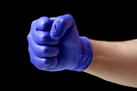 Fist of a man in a blue latex glove close-up on a black background.の写真素材