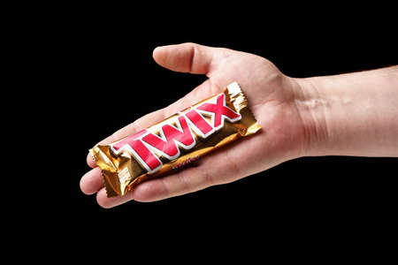 A man offers a Twix chocolate bar, hand holding a chocolate bar close-up, black background