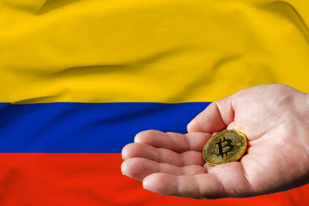 Golden bitcoin coin in man's hand, Colombia flag in the background.の写真素材