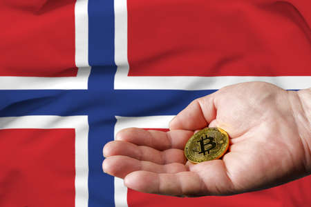 Golden bitcoin coin in man's hand, Norway flag in the background.の写真素材