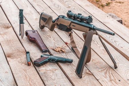 Scout bolt rifle, APS pistol, knife and cartridges on a wooden platform. Side viewの写真素材