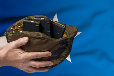 A military helmet with cartridges and magazines for a rifle in the hands of a man against the background of the flag of Somalia. The concept of selling weapons or military assistanceの写真素材