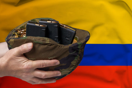 A military helmet with cartridges and magazines for a rifle in the hands of a man against the background of the flag of Colombia. The concept of selling weapons or military assistanceの写真素材