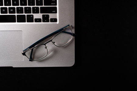Glasses and a laptop on a black table, backlight. close-up.の写真素材
