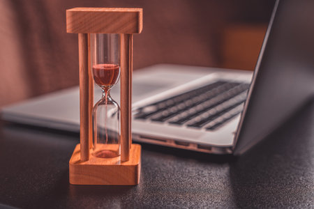 Laptop and hourglass on the desktop. Time management concept.