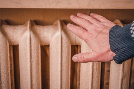 Man's hand and radiator, close-up. Man warming his hand over a heaterの写真素材