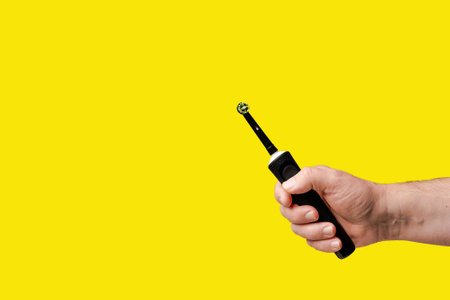 A man holding an electric toothbrush. A black toothbrush in the mans hand against a yellow backgroundの写真素材