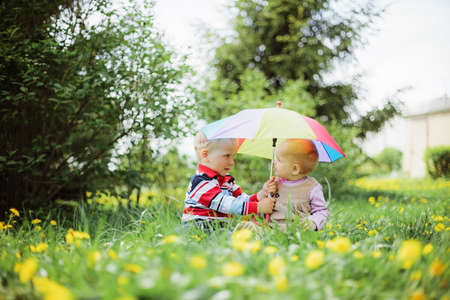 two babies sitting in the garden holding rainbow umbrella
の写真素材