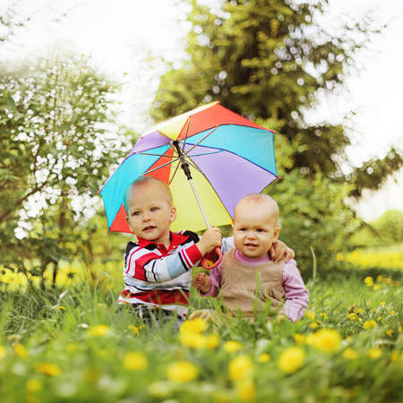 two babies sitting in the garden holding rainbow umbrella
の写真素材