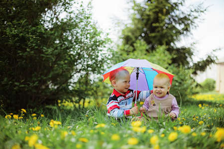 two babies sitting in the garden holding rainbow umbrella
の写真素材