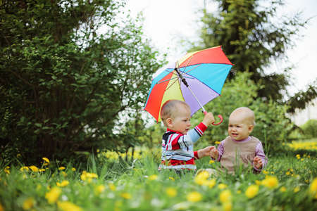 two babies sitting in the garden with rainbow umbrella
の写真素材