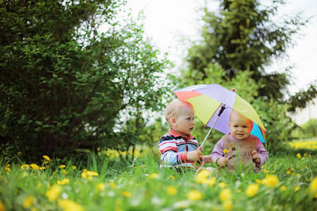 two babies sitting in the garden with rainbow umbrella
の写真素材