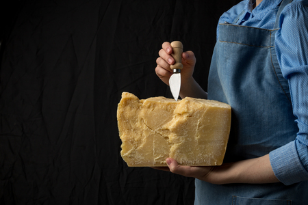 Woman holding knife and a slice of parmesan cheese on black background. Studio shotの写真素材